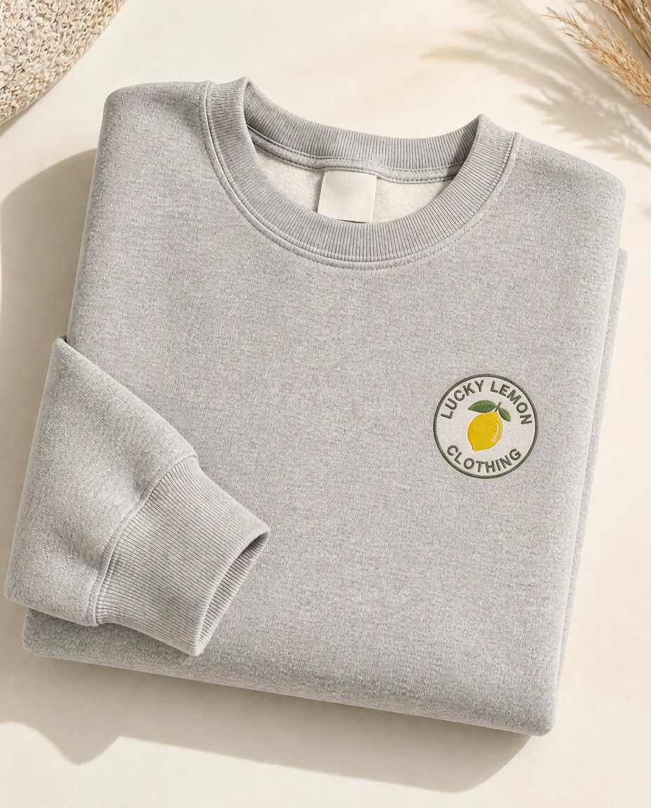 Lucky Lemon women's heather gray crewneck sweatshirt, folded, with the lemon badge printed at the top left